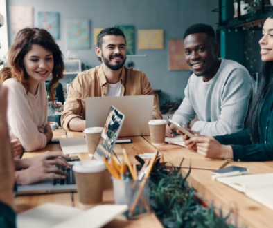 A diverse, smiling team of Impimpi Tech professionals collaborating during a meeting around a wooden office table.