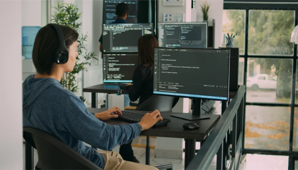 An Impimpi Tech software engineer wearing headphones and writing code on a desktop computer in an office.